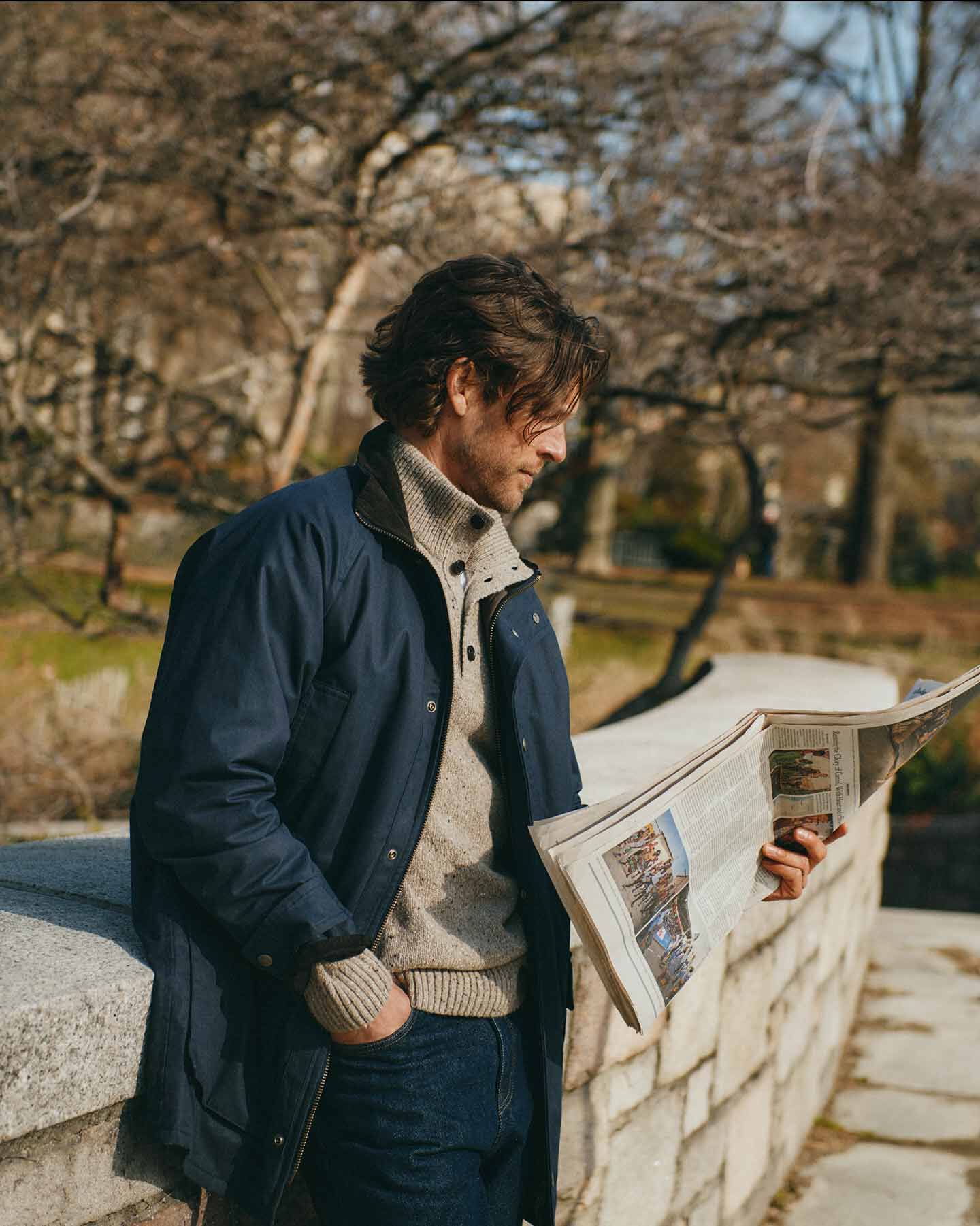 Men in dark blue Gant double decker reading newspaper in a park